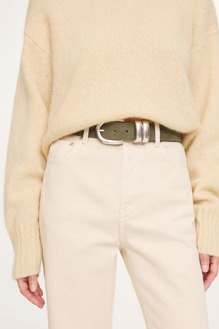 By Malene Birger Zoira Suede Belt in Deep Lichen Green, featuring a wide suede strap and a signature curved silver buckle. This adjustable one-size belt is designed to cinch the waist or sit on the hips for a sophisticated, textured look.