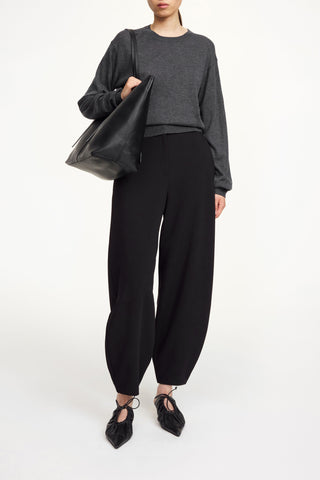 By Malene Birger Carlien Trousers in black, featuring a modern barrel silhouette and structured scuba-like fabric. These high-waisted tailored pants include pressed creases and side pockets, making them a versatile staple for a professional capsule wardrobe.