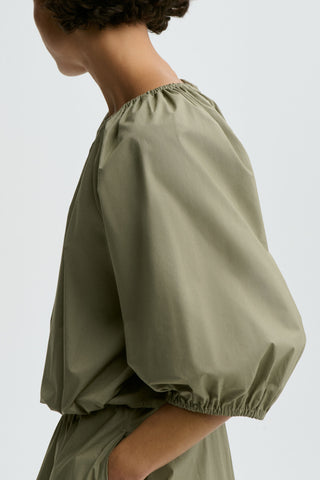 By Malene Birger Lelow Blouse in Deep Lichen Green, featuring a voluminous silhouette in crisp organic cotton. This versatile top includes an elasticated neckline for on or off-the-shoulder styling, with puff sleeves and an elasticated hem.