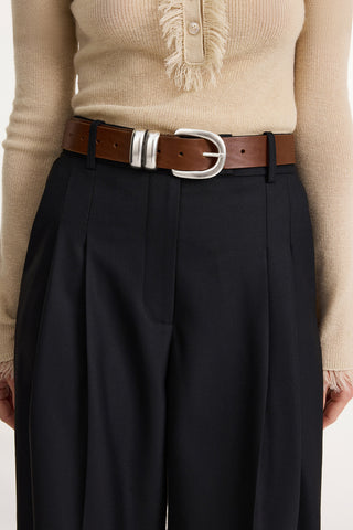 By Malene Birger Zoira Belt in Dark Brown, a luxury leather waist belt featuring a sculptural silver-tone buckle and distinctive double-loop hardware. This elevated designer accessory adds a polished, waist-defining touch to oversized blazers or flowing dresses.