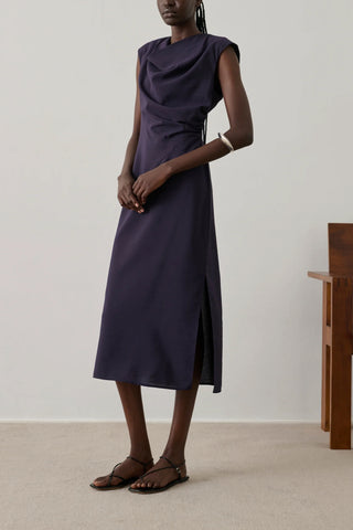 Soeur Eugenie Dress in Violet Fonce, a sophisticated sleeveless midi dress featuring a draped cowl neckline and elegant side-gathering. This premium designer piece in a deep plum purple offers a sleek, feminine silhouette that transitions perfectly from professional gallery openings to formal evening events.